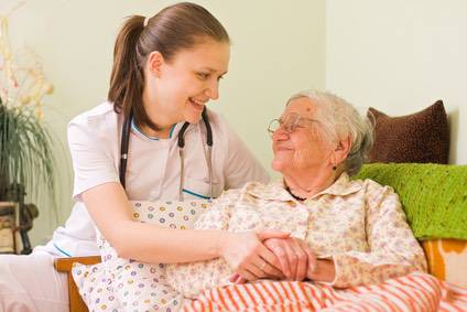 A young doctor / nurse visiting an elderly sick woman holding her hands with caring attitude.